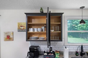 A kitchen with a dark wooden cabinet, a coffee maker, and a window with a view of greenery.