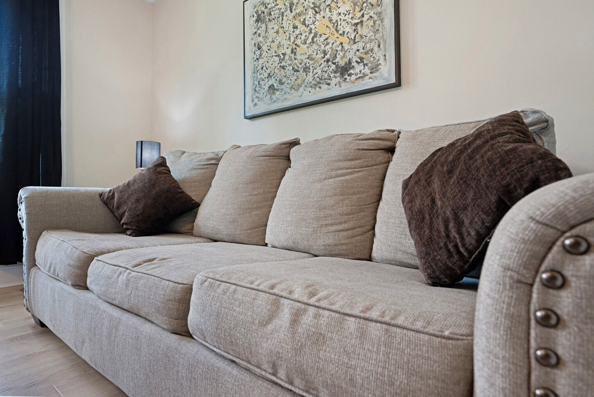 A beige sofa with multiple cushions, a lamp, and a framed abstract artwork on the wall.