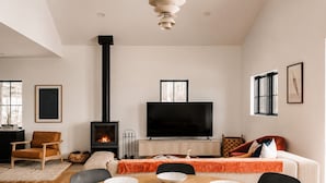 A modern living room with a fireplace, a flat-screen TV, and a dining area with a table set for four. - Hot Tub, Fire Pit, Views & 14 Acres | Onyx Ridge (Jeffersonville)