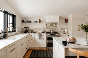 A modern kitchen with white cabinetry, a marble backsplash, a gas stove, and a built-in oven. - Hot Tub, Fire Pit, Views & 14 Acres | Onyx Ridge (Jeffersonville)
