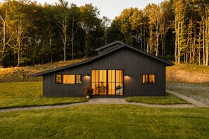 Una moderna casa a due piani con un'ampia porta d'ingresso in vetro, immersa in un prato curato e una fitta foresta.
