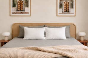 Un letto con copripiumino grigio, due cuscini, una coperta lavorata color beige e due abat-jour.