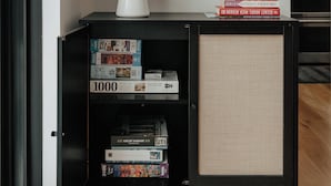 A black bookshelf with a white vase of dried flowers on top, a small stack of books, and a woven basket. - Hot Tub, Fire Pit, Views & 14 Acres | Onyx Ridge (Jeffersonville)