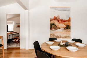 A modern dining area with a round table, white bowls, and a painting on the wall.
