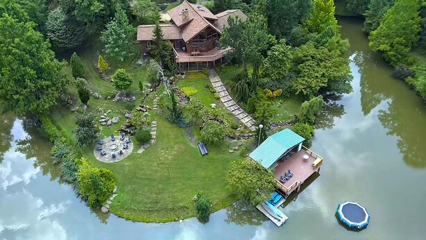 A large house with a deck and a dock extending into a lake, surrounded by lush greenery. - Grace Woods - Private Lake - Dock -Large Groups - 3 Entire Homes-Lake House (Rising Sun)
