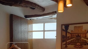 Una stanza con soffitto in legno, una finestra che si affaccia su un cortile interno, un appendiabiti sospeso e un aspirapolvere.