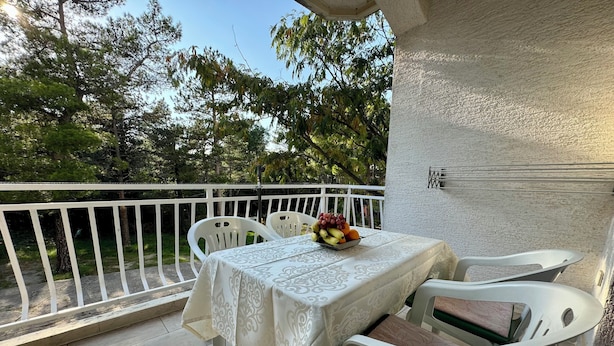 Een balkon met een tafel en stoelen, een schaal fruit en uitzicht op bomen.
