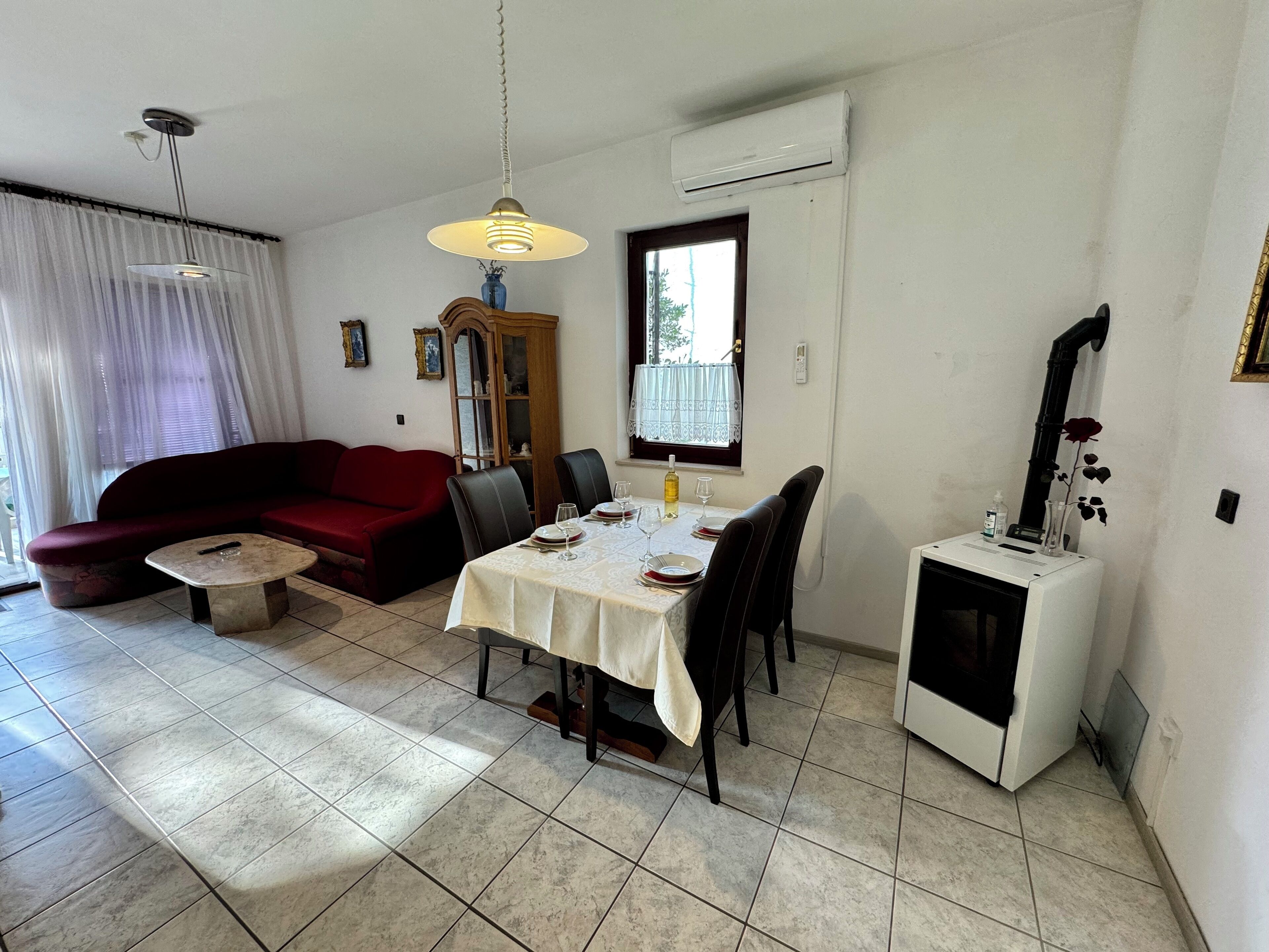 Een woonkamer met een rode bank, een eettafel voor vier personen en een klein bijzettafeltje. Er is een raam met uitzicht op groen.