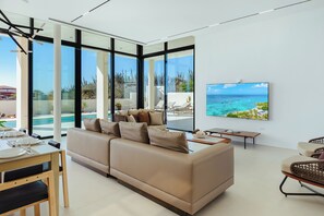 Una sala de estar moderna con un sofá grande, un comedor y un televisor mostrando una escena de playa.