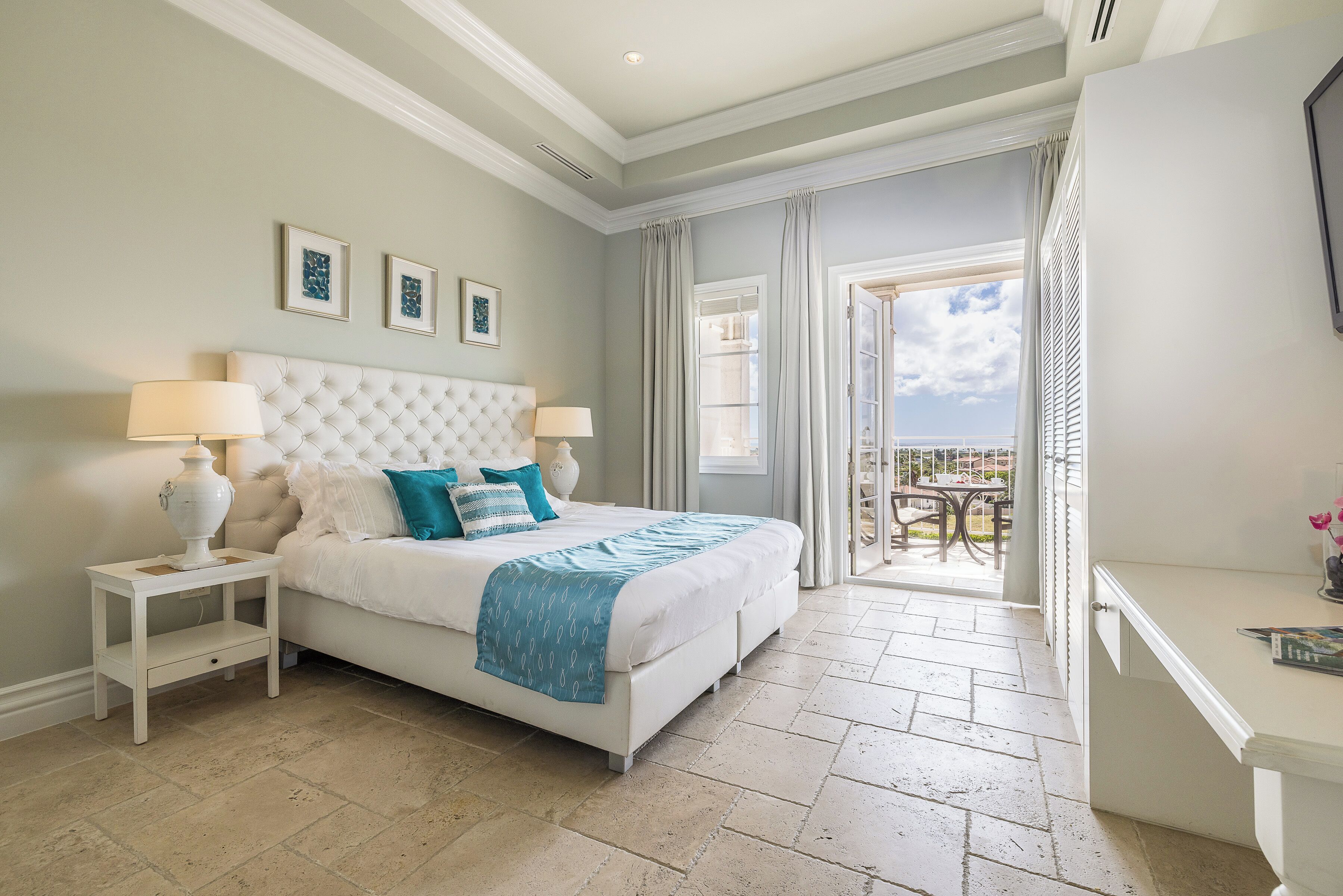A bedroom with a large bed, two bedside tables, a dresser, and a balcony with a view.