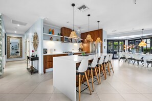 Una cocina moderna con una isla central, taburetes de bar, luces colgantes y un espejo grande.