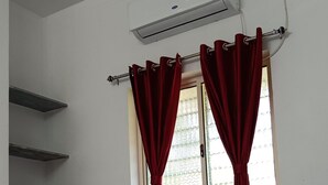 A hotel room with a bed, a window with red curtains, a wall-mounted air conditioner, and a ceiling with recessed lighting. - De Capital Hotel (Vanur)