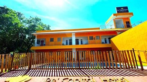 The exterior of De' Capital Hotel with a prominent entrance sign, a wooden fence, and a clear sky. - De Capital Hotel (Vanur)