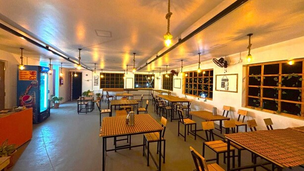 A spacious indoor dining area with multiple tables and chairs, a vending machine, and large windows along one wall. - De Capital Hotel (Vanur)