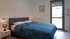 Un dormitori amb llit, làmpades de nit, un quadre al mur i una porta que dóna a l'exterior.