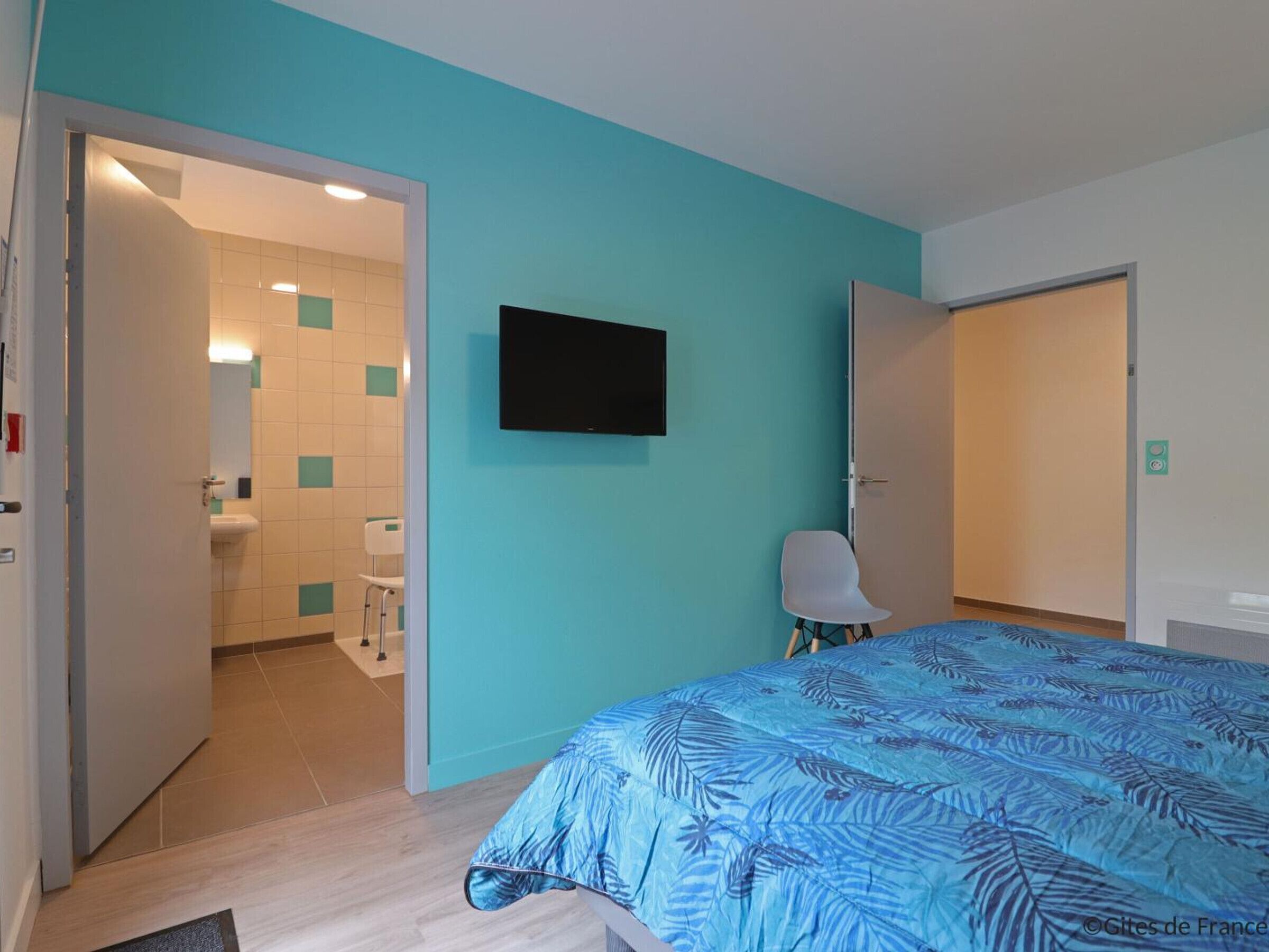 A hotel room with a bed, a TV mounted on the wall, and a bathroom visible through an open door.
