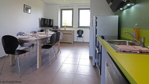 Una cuina moderna amb microones integrat, un rentapeus i una finestra. Hi ha una zona de menjador amb una taula preparada per a quatre, cadires i un televisor penjat a la paret.