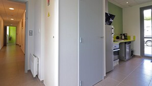 Un passadís que condueix a una zona de cuina, amb una paret verda, una porta blanca i un radiador.