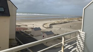 Blick auf einen Strand vom Balkon mit Geländer, feinem Sand und dem Meer im Hintergrund.
