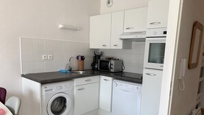 Eine kompakte Küche mit weißen Schränken, einer Waschmaschine, einer Mikrowelle und einem Spülbecken.
