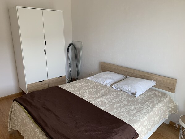 A bedroom with a bed, a wardrobe, and a vacuum cleaner.
