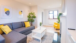 Un salon moderne avec un canapé gris, des coussins jaunes, une table basse blanche et une œuvre d’art abstraite accrochée au mur.