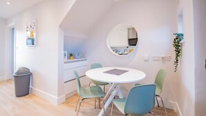 Un coin repas comprenant une table ronde, quatre chaises, une poubelle, un miroir et une plante.