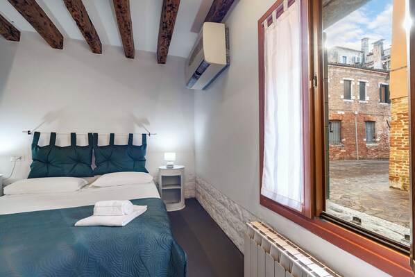 A bedroom with a bed, bedside table, and a window with a view of a courtyard. - Ca' Nova II by Wonderful Italy (Venice)