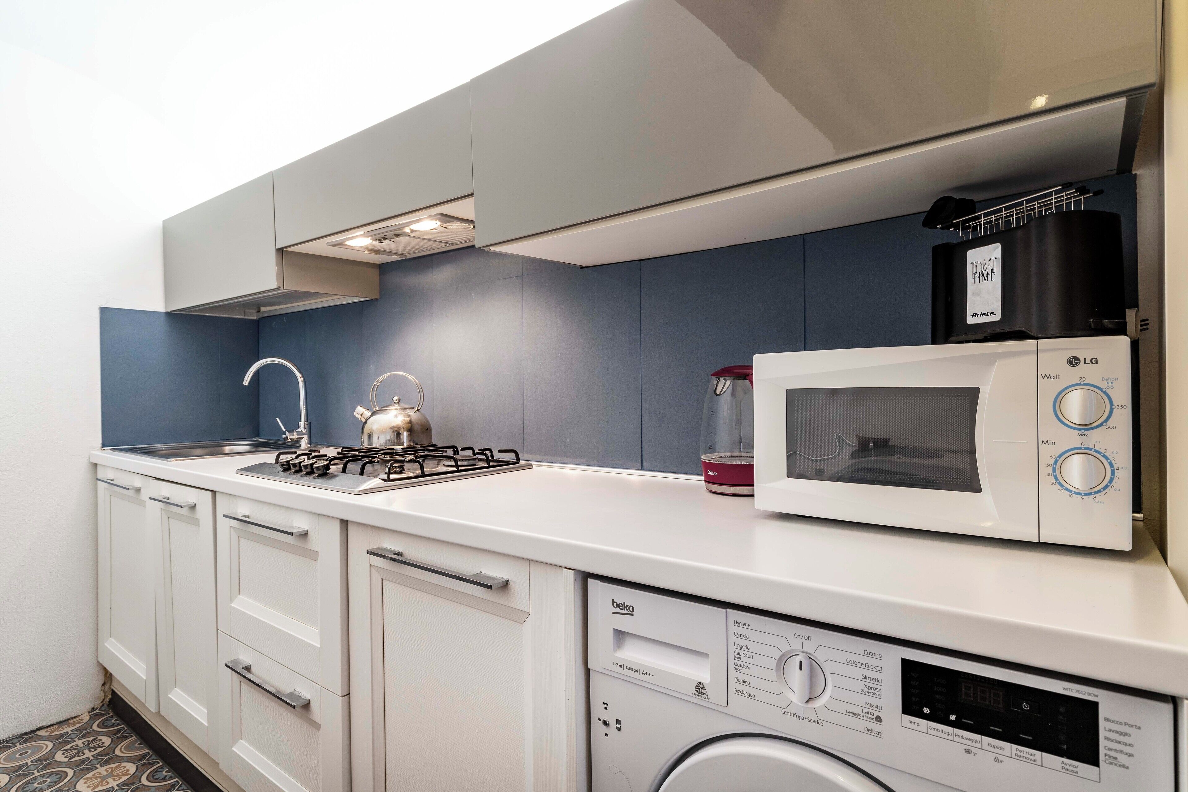 A compact kitchen with a microwave, kettle, and a washing machine.