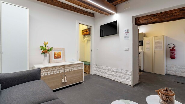 Una habitación de hotel moderna con un sofá gris, un mueble de madera y un televisor de pantalla plana montado en la pared.