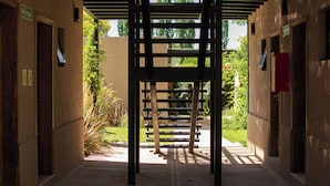 Un couloir avec des bancs en bois, des portes et une vue sur la verdure à l’extérieur.