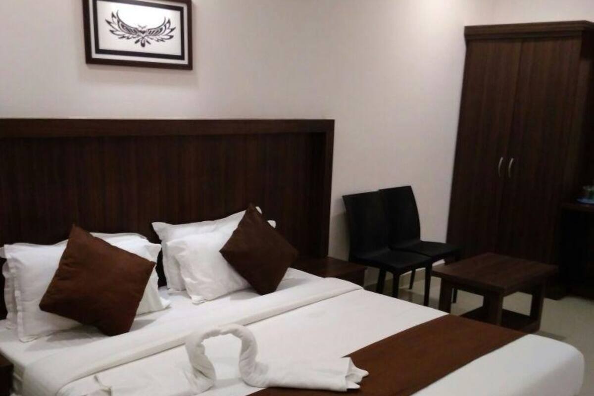 A neatly made bed with white and brown bedding, a framed picture on the wall, and a wooden wardrobe.