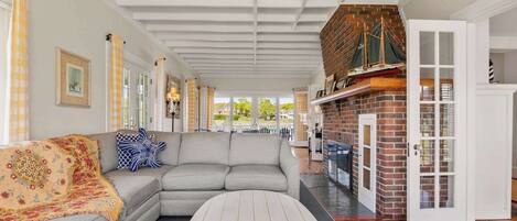 A spacious living room with a grey sectional sofa, a round coffee table, and a brick fireplace.