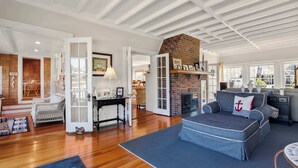 A spacious living room with a fireplace, wooden flooring, and a view of the outdoors. - Waterfront, Walk to Beach! (Barnstable)
