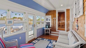 A cozy room with a view of the water, a wicker sofa, and a small table with decorative items. - Waterfront, Walk to Beach! (Barnstable)
