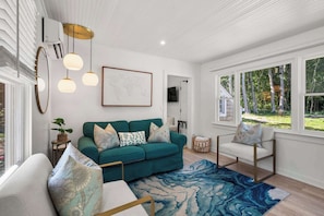 A living room with a teal sofa, patterned cushions, a blue and white rug, and a framed world map on the wall. - Private Hot Tub, Near Dennis Pond (Yarmouth)