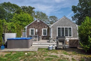 A two-story house with a covered patio area, a hot tub, and outdoor furniture.