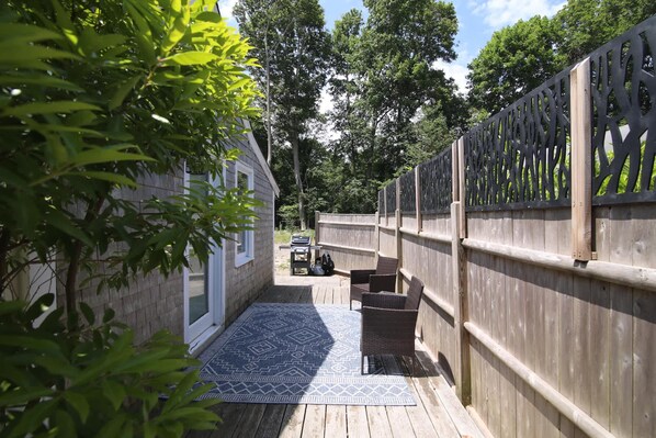 A wooden deck with a patterned rug, a grill, and wicker chairs. - Adorable Updated Cottage, Walk to Water! (Yarmouth)