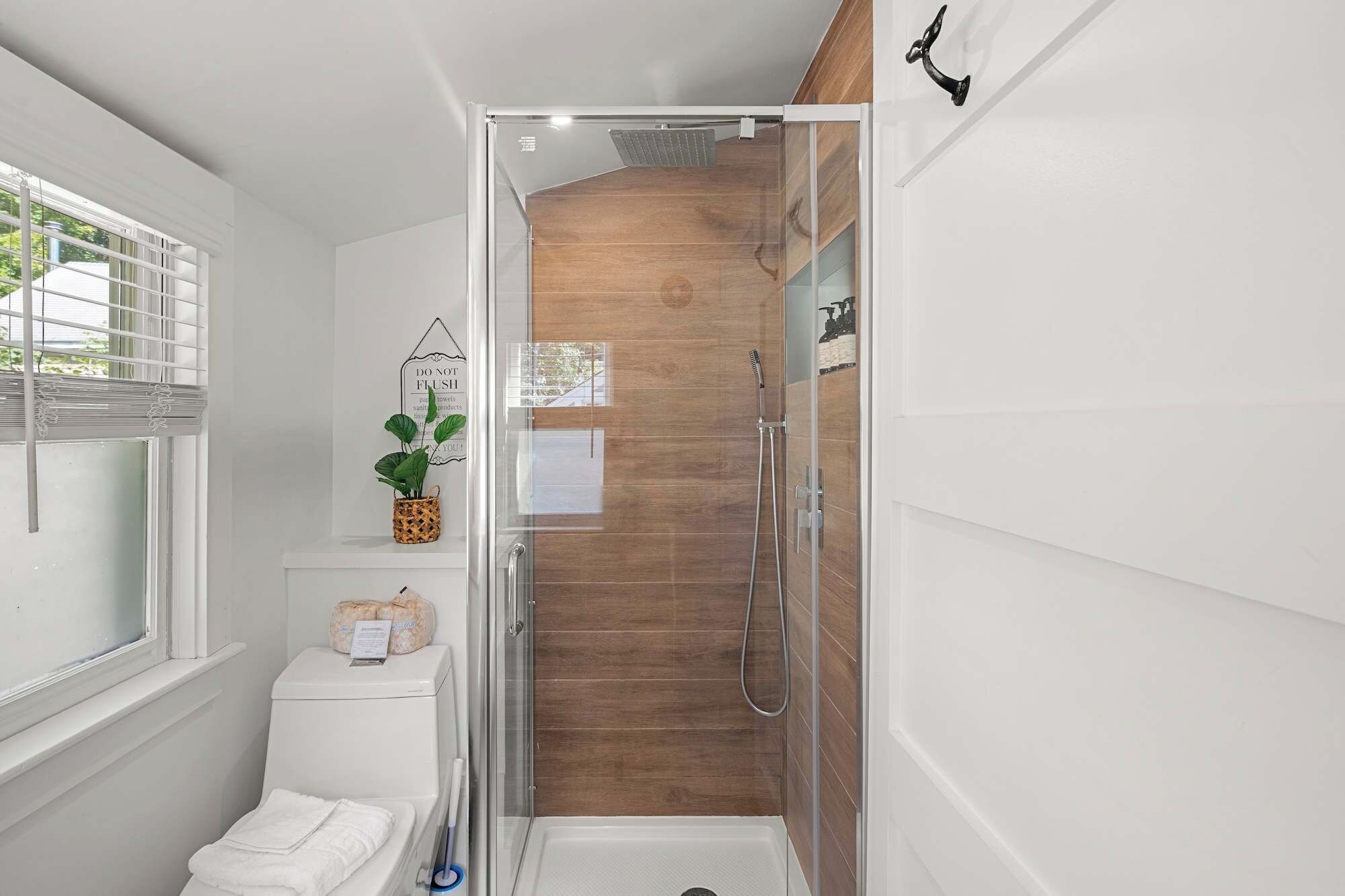 Ein Badezimmer mit Dusche, Toilette und einem Fenster mit Jalousien.