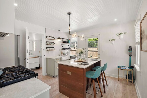 A modern kitchen with a central island, bar stools, pendant lighting, and a view to the outdoors. - Adorable Updated Cottage, Walk to Water! (Yarmouth)