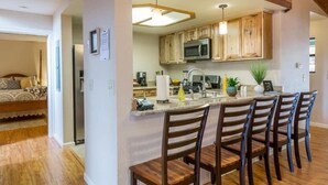 A modern kitchen with wooden cabinets, a central island with bar stools, and a built-in microwave. - Sierra Grand Inside Yosemite (Wawona)