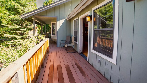 A wooden deck with a railing, a covered porch, and a large window. - Sierra Grand Inside Yosemite (Wawona)