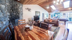 A spacious living area with a stone wall, wooden ceiling, and a dining table with chairs. - Sierra Grand Inside Yosemite (Wawona)