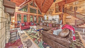 A spacious living area with a high ceiling, wooden beams, and a large window.