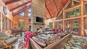 A spacious lodge with a high ceiling, a fireplace, leather seating, and large windows.