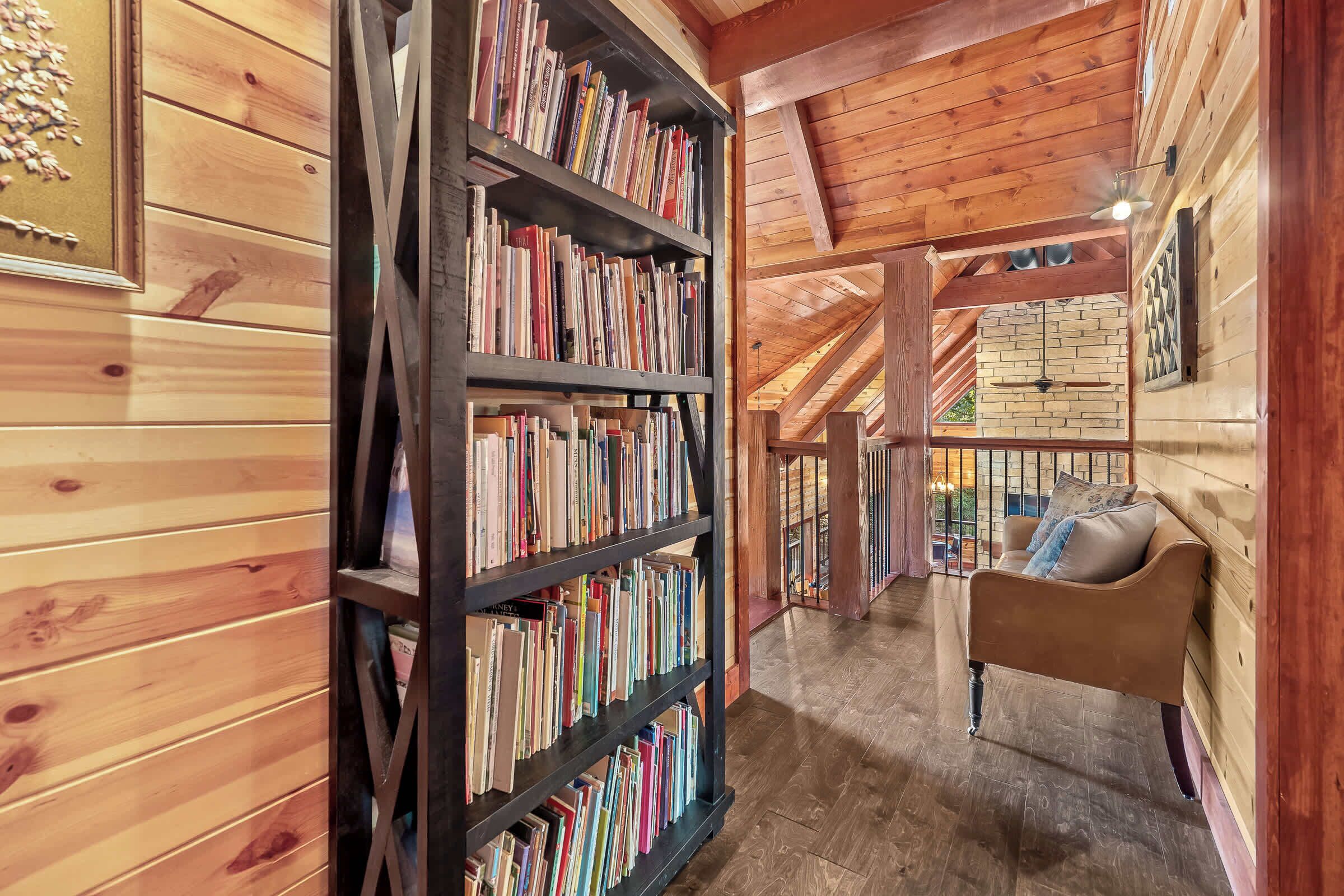 A wooden interior with a bookshelf, a sofa, and a view of the outside.