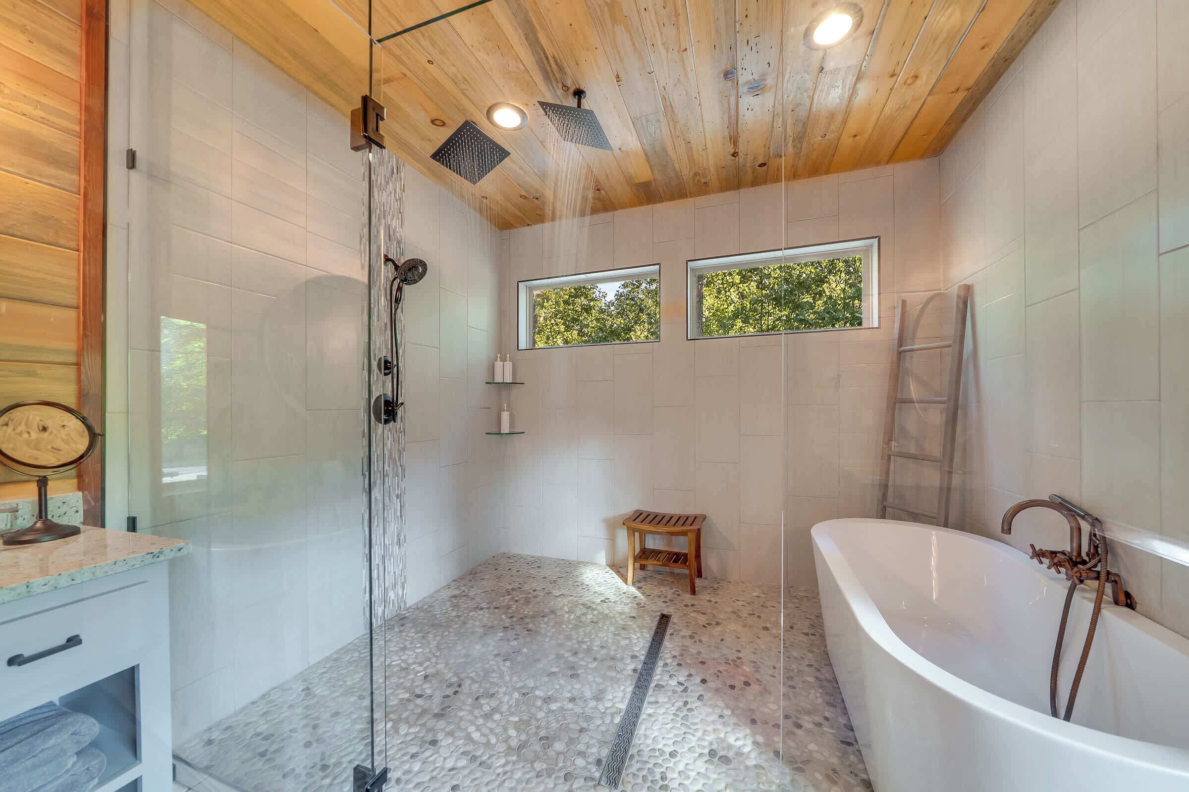 Un baño moderno con una bañera independiente, cabina de ducha de vidrio y un banco de madera.