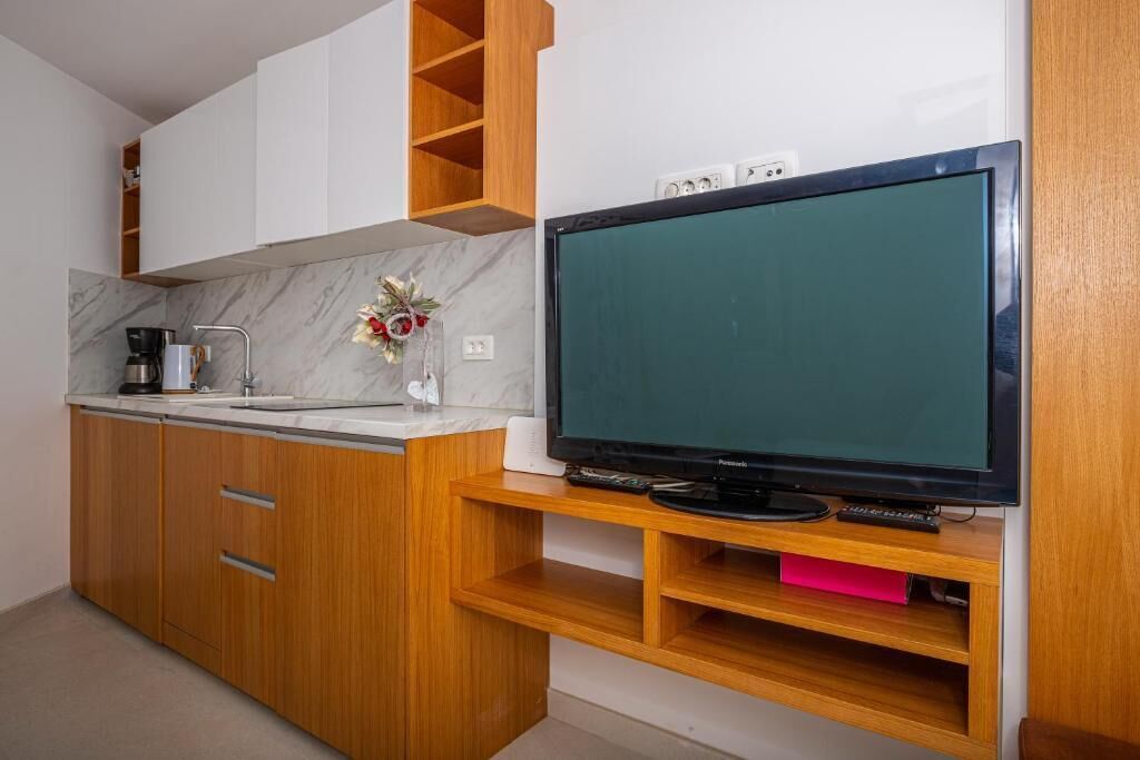 A modern kitchen with wooden cabinets, a marble countertop, a built-in TV, and a coffee maker.