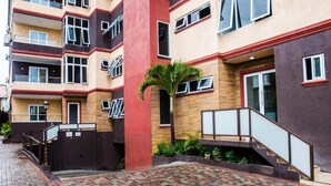 A multi-story residential building with a brick-paved courtyard, a palm tree, and a staircase leading to the entrance.