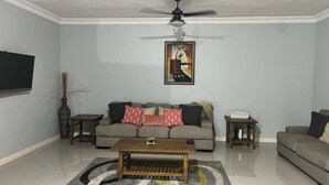 A living room with a grey sofa, a coffee table, a painting on the wall, and a ceiling fan.